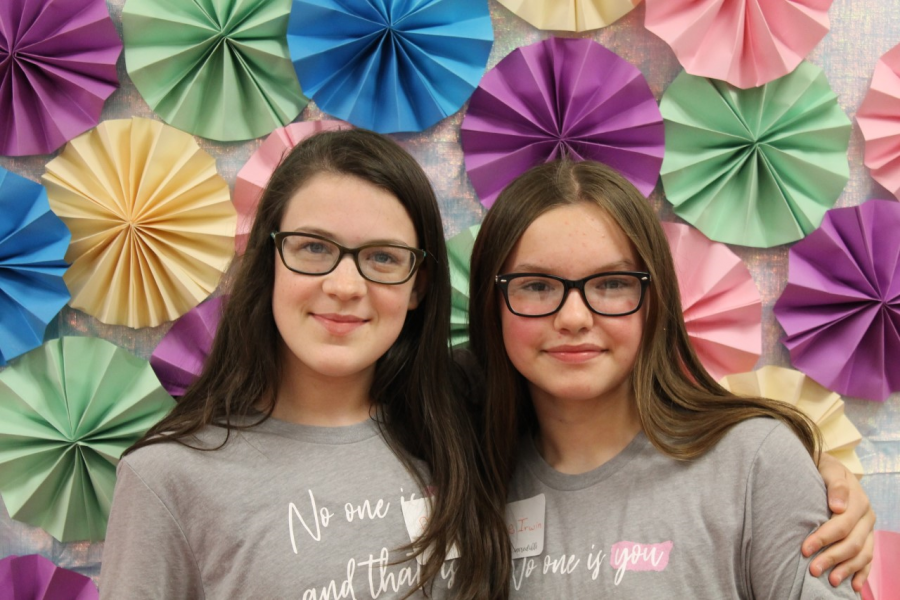 Two students pose in front of a paper flower backdrop for a picture.